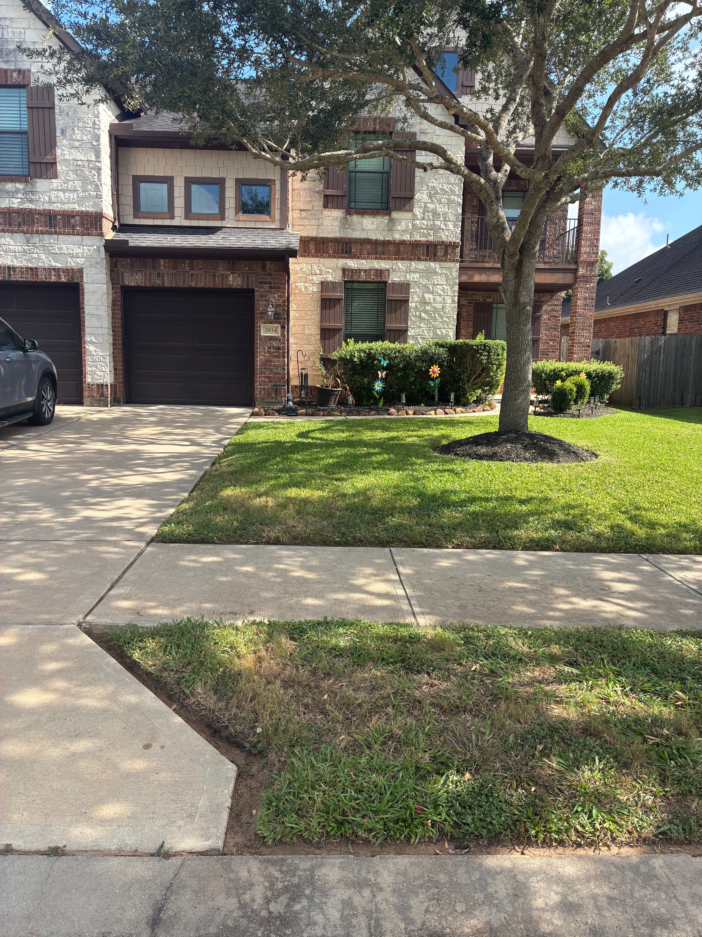 Two-story brick and stone home with manicured front lawn and garden beds