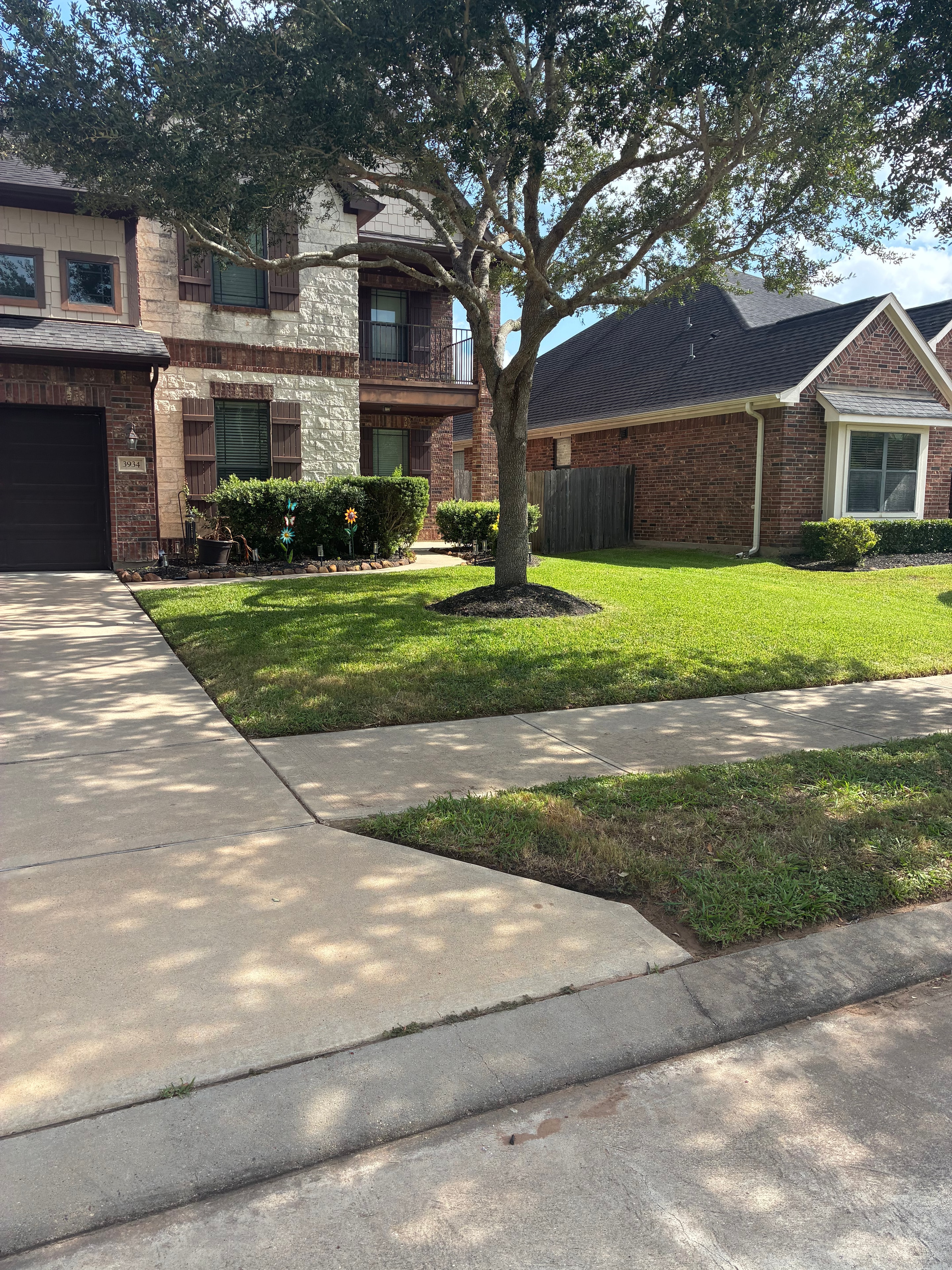 Two-story brick home with lush mowed front lawn and tree ring